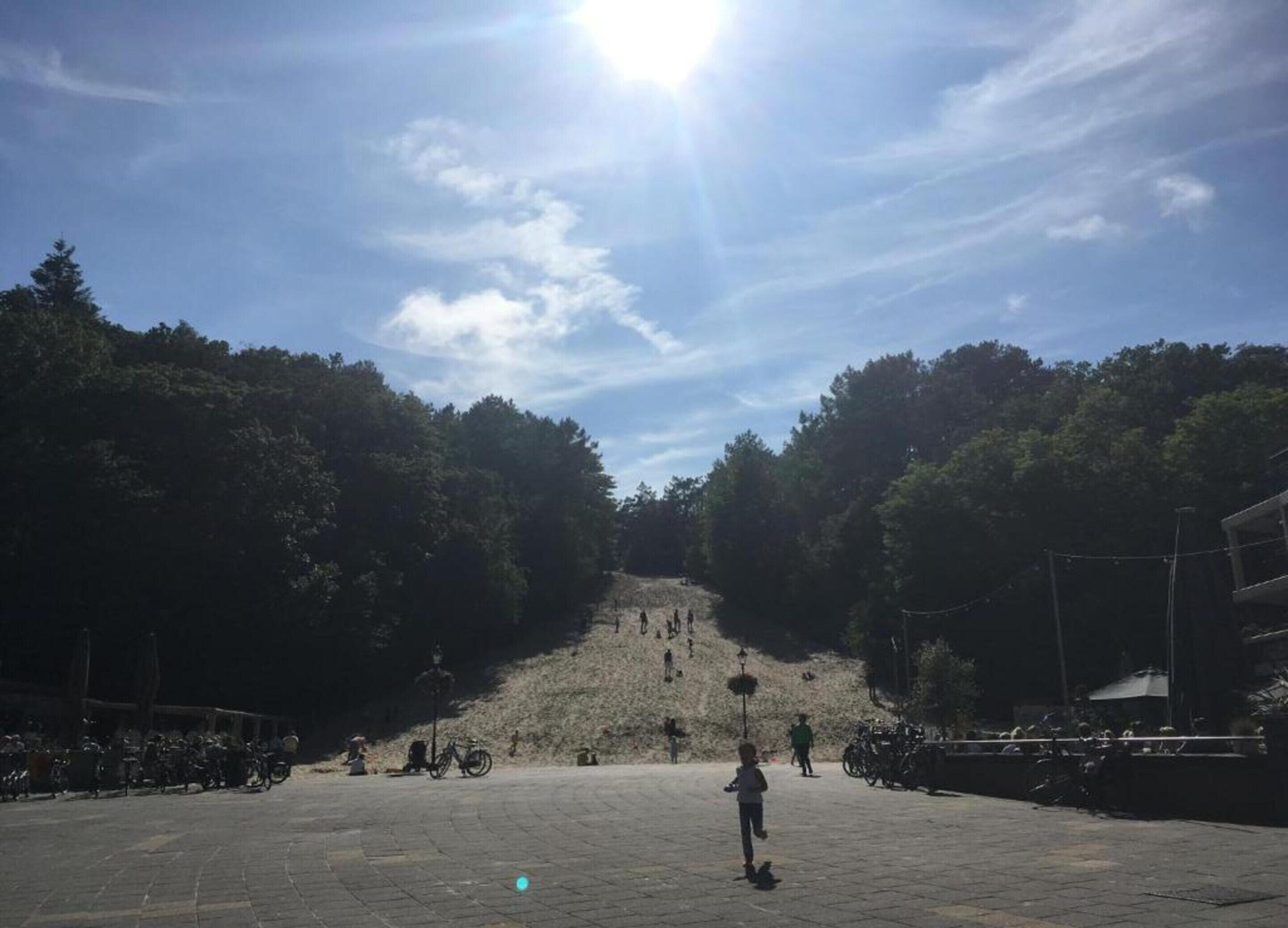 A paved plaza with a large hill in the background, surrounded by trees.