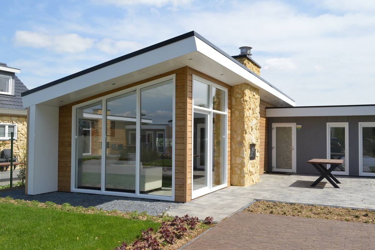 A modern building with large glass doors, a stone exterior, and a patio area with a table.