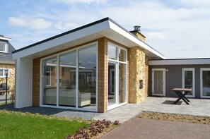 A modern building with large glass doors, a stone exterior, and a patio area with a table. - Bemelen Holiday Home for 6 (Bemelen)
