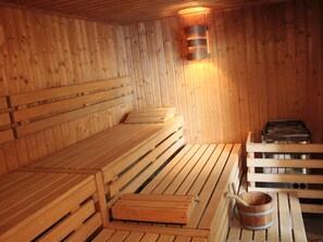 Una sauna de madera con bancos y un asiento, un cubo de madera y un calentador de sauna.