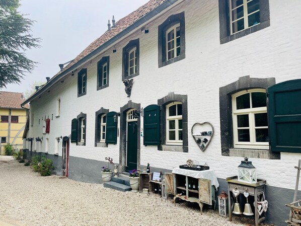 A white building with green shutters and a heart-shaped window decoration.