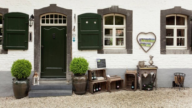 A white building with green shutters, a door, and windows. There are potted plants, wooden crates, and a heart-shaped decoration on the wall. - Scenic Gulp Valley Stay (Slenaken)
