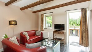 A living room with a red leather sofa, a glass coffee table, a flat-screen TV on a wooden stand, and a view of a garden through a window. - Scenic Gulp Valley Stay (Slenaken)