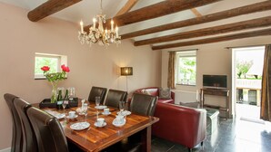 A dining area with a wooden table set for six, surrounded by leather chairs. A chandelier hangs from the ceiling, and there is a red leather sofa in the background. - Scenic Gulp Valley Stay (Slenaken)