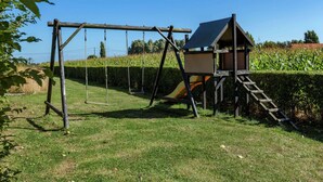 A wooden swing set with a slide, a small wooden house, and a clear blue sky.