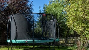 A trampoline with a safety net, surrounded by a wooden fence and trees.