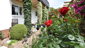 A white house with a balcony, surrounded by a garden with various plants and flowers. - Apartment With Parasol in Sudstadt (Rostock)