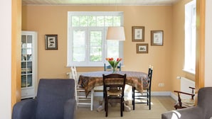 A dining area with a table set for four, surrounded by chairs, a window with a view of greenery, and framed pictures on the wall. - Chic Apartment in Hessisch Oldendorf (Hessisch Oldendorf)
