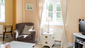 A cozy living room with a grey armchair, a white side table with a lamp, a television, and a small cabinet. - Chic Apartment in Hessisch Oldendorf (Hessisch Oldendorf)
