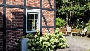A half-timbered building with a white window, a garden with hydrangeas, and a wooden fence. - Chic Apartment in Hessisch Oldendorf (Hessisch Oldendorf)