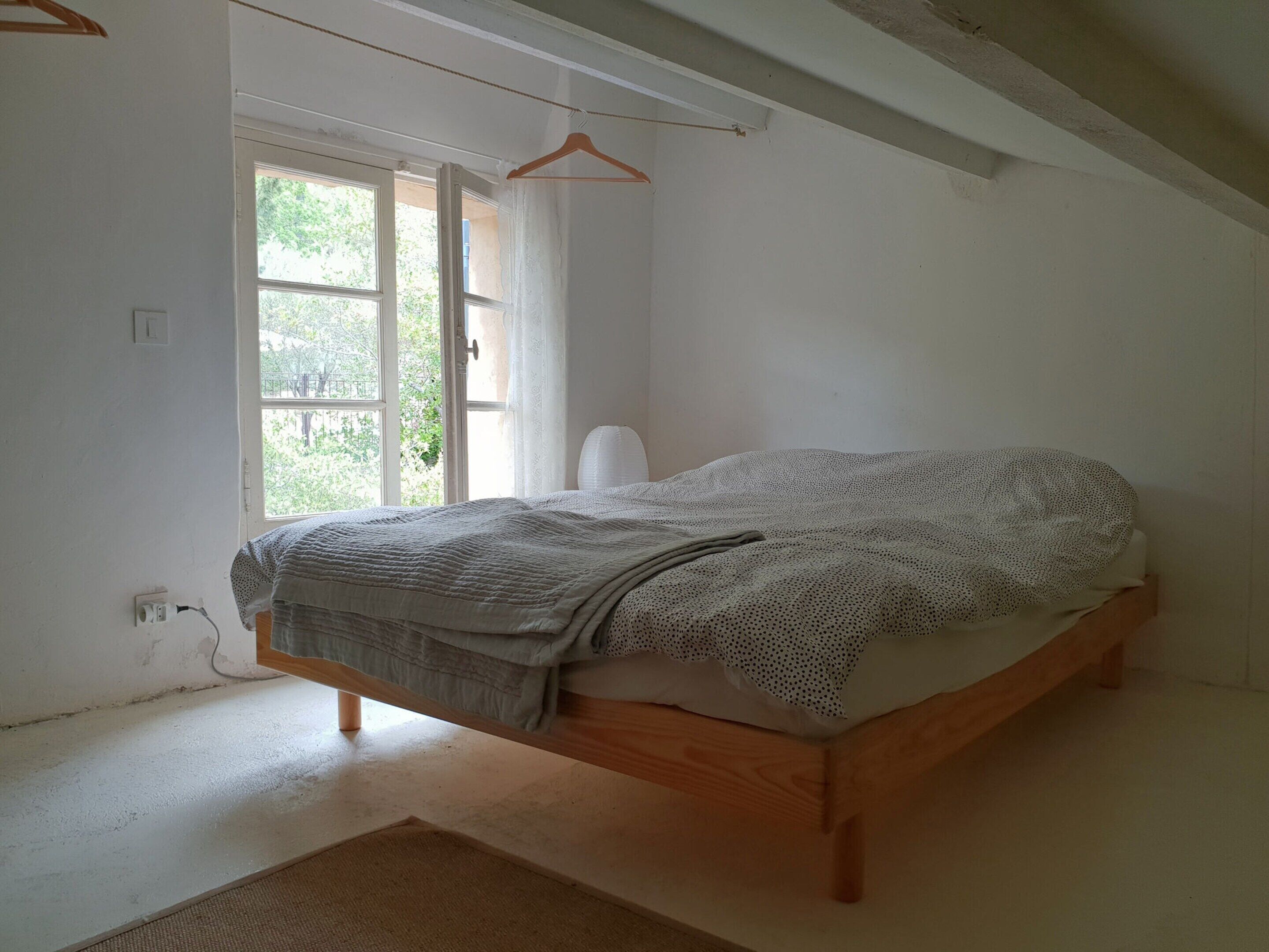Une chambre avec un lit en bois, une fenêtre avec des rideaux et un luminaire suspendu.