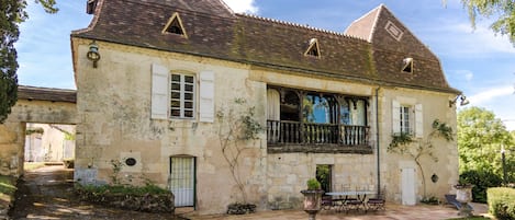 A stone house with a balcony, a garden, and a paved patio.