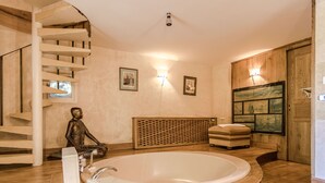 Une salle de spa dotée d’une grande baignoire, d’un plancher en bois, d’un escalier en colimaçon et d’œuvres d’art accrochées au mur.