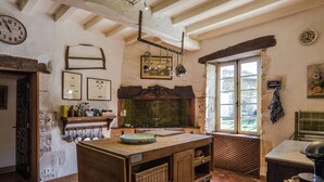Une cuisine rustique avec un îlot central en bois, des ustensiles de cuisine suspendus et une fenêtre donnant sur un paysage agréable.