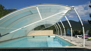 Ein Schwimmbecken mit Glasverkleidung, umgeben von Liegestühlen und einem Kiesdeck.