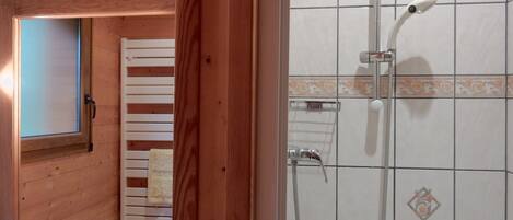 A bathroom with a wooden interior, a sink, a mirror, and a shower with a handheld showerhead.