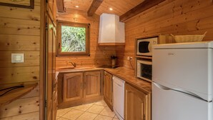 Ein Holzblock-Interieur mit Küchenbereich, inklusive Holzausstattung, Spüle, Fenster mit Blick auf Bäume und Decke mit sichtbaren Balken.