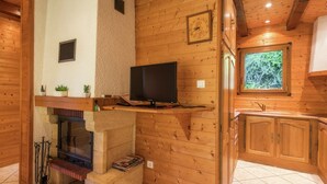 Ein Holzinterieur mit Kamin, Fernseher auf einem Regal und einem Fenster mit Blick auf Grünflächen.