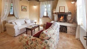 A cozy living room with a fireplace, a sofa, a floral-patterned armchair, and a wooden ceiling. - Authentic Holiday Home in Barban With Swimming Pool (Rasa)