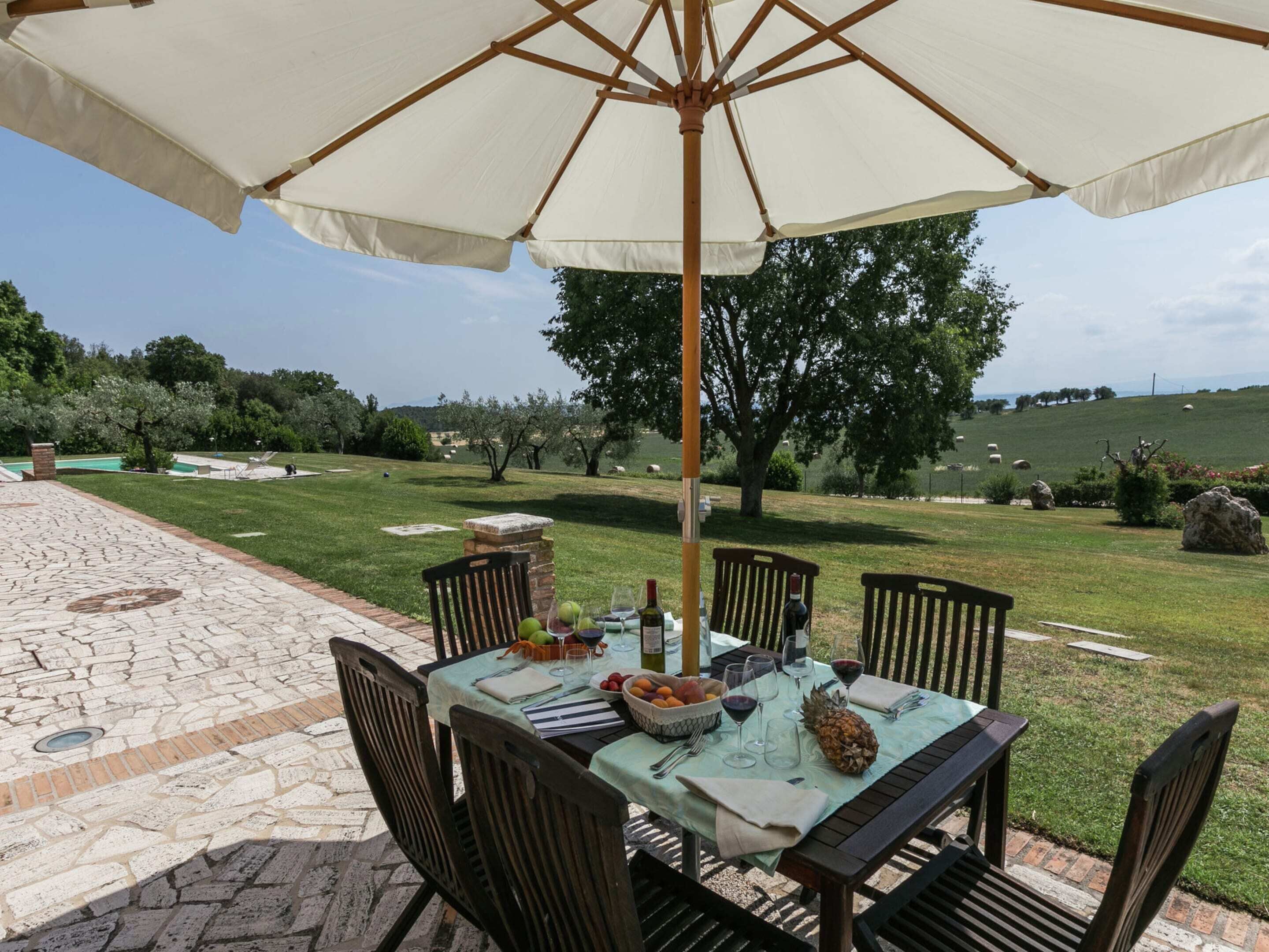 An outdoor dining area with a table set for four, surrounded by chairs, under a large umbrella.