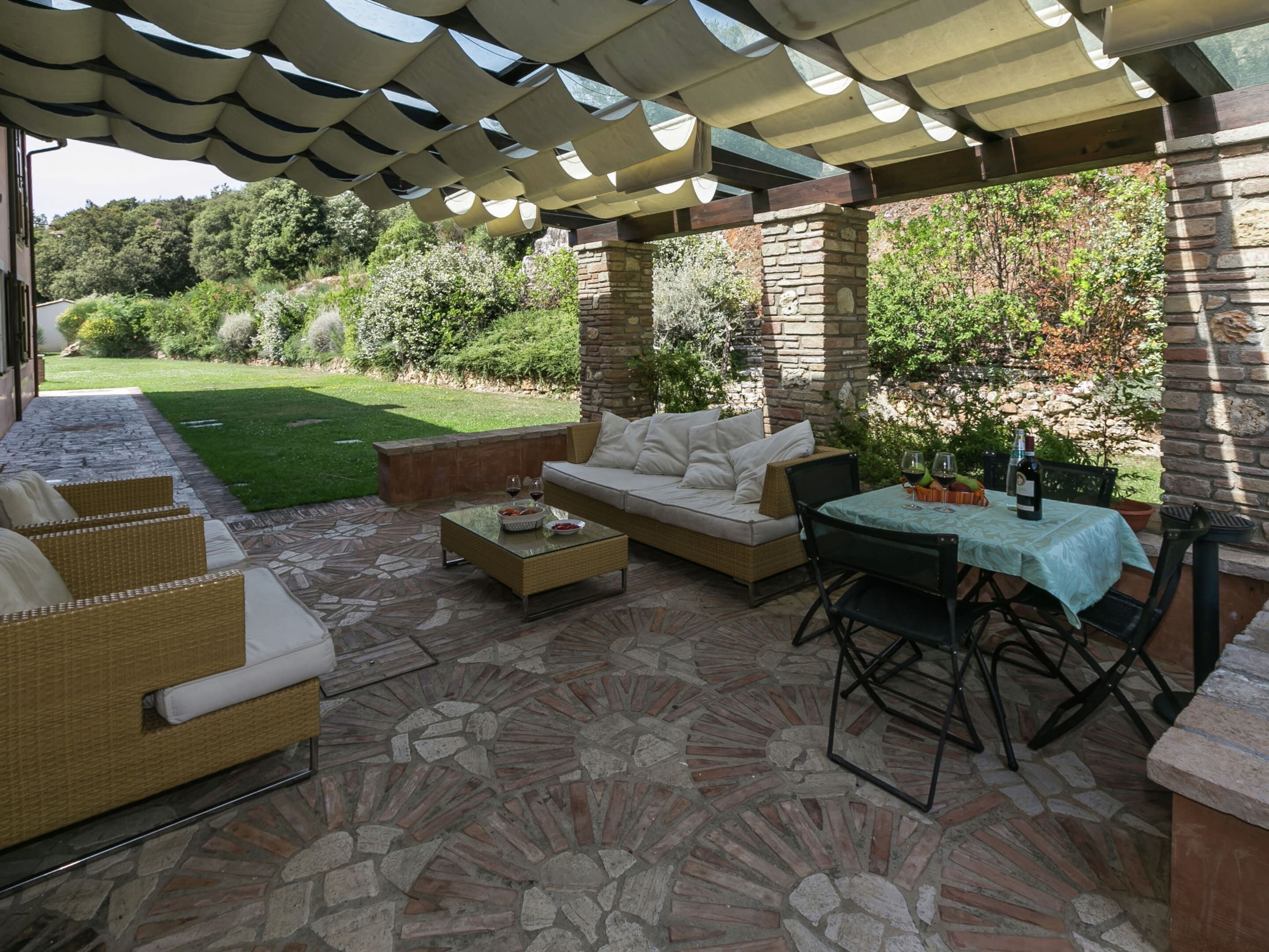 An outdoor patio area with a stone floor, wicker furniture, a table with wine glasses, and a stone wall.