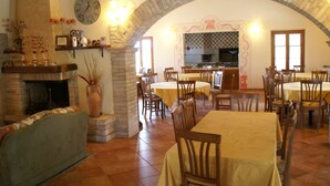 A dining area with multiple tables and chairs, a stone fireplace, and a kitchen in the background. - Holiday Home in Bettona With Pool & Near Assisi (Bettona)