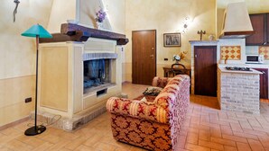 A cozy living room with a fireplace, a sofa, a lamp, and a kitchen area with a microwave and gas stove. - Luxury, Modern Apartment With Pool and Stunning Views (Narni)