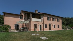 A two-story building with a balcony, a dining area with outdoor furniture, and a well-maintained lawn. - Luxury, Modern Apartment With Pool and Stunning Views (Narni)