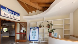A reception area with a wooden ceiling, a reception desk, a bulletin board, and potted plants. - Comfort in Lido Delle Nazioni (Comacchio)