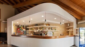 A modern bar area with a curved counter, hanging pendant lights, and shelves stocked with bottles. - Comfort in Lido Delle Nazioni (Comacchio)