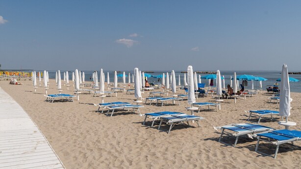A beach with rows of sun loungers and umbrellas, a wooden walkway, and a clear sky. - Comfort in Lido Delle Nazioni (Comacchio)
