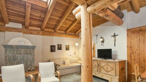 Ein gemütliches Zimmer mit Holzbalkendecke, einer Couch, zwei Stühlen, einem Schrank und einem Fernseher.