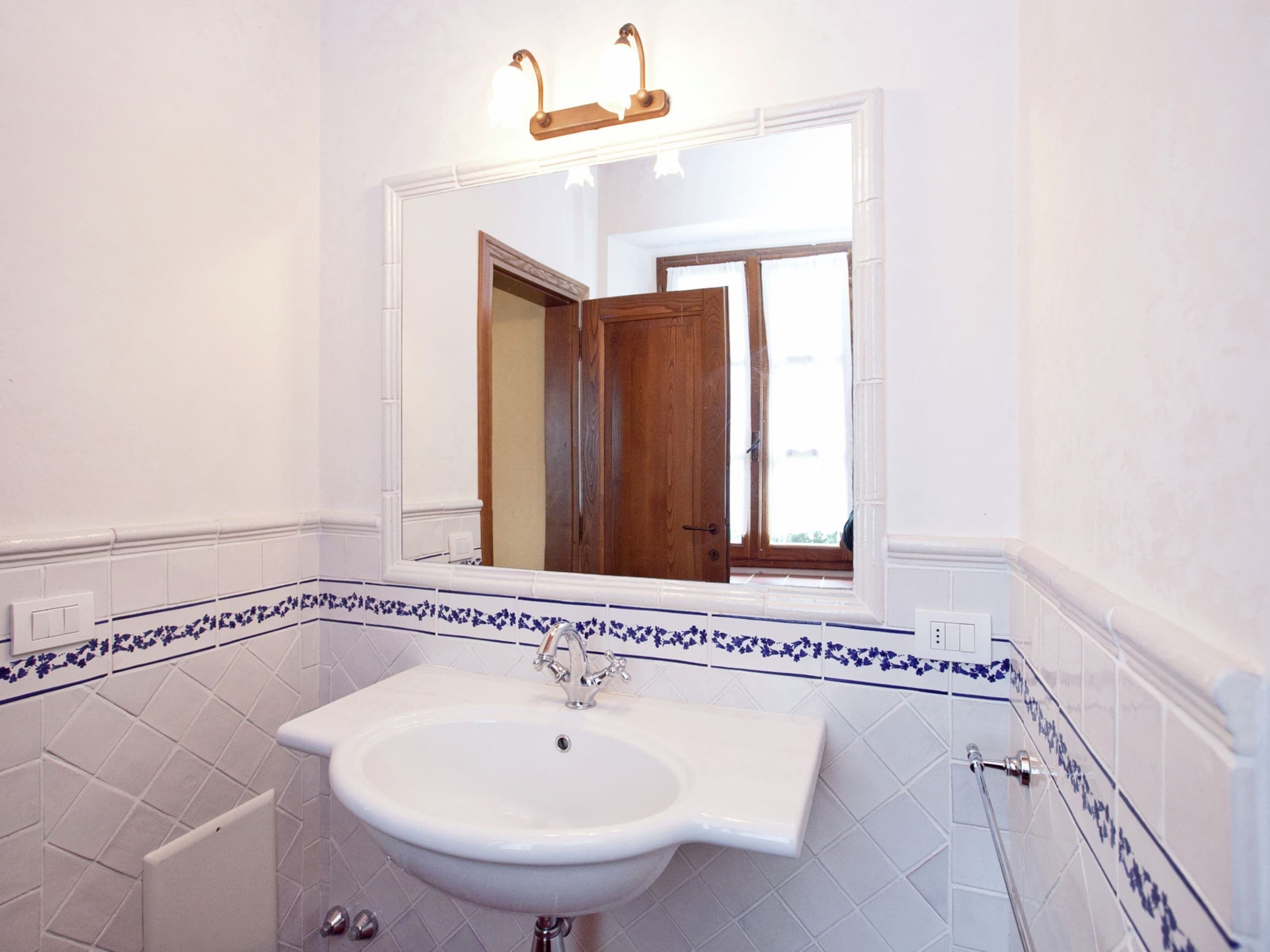 A bathroom with a white sink, a mirror above it, and a window with a wooden door visible in the reflection.
