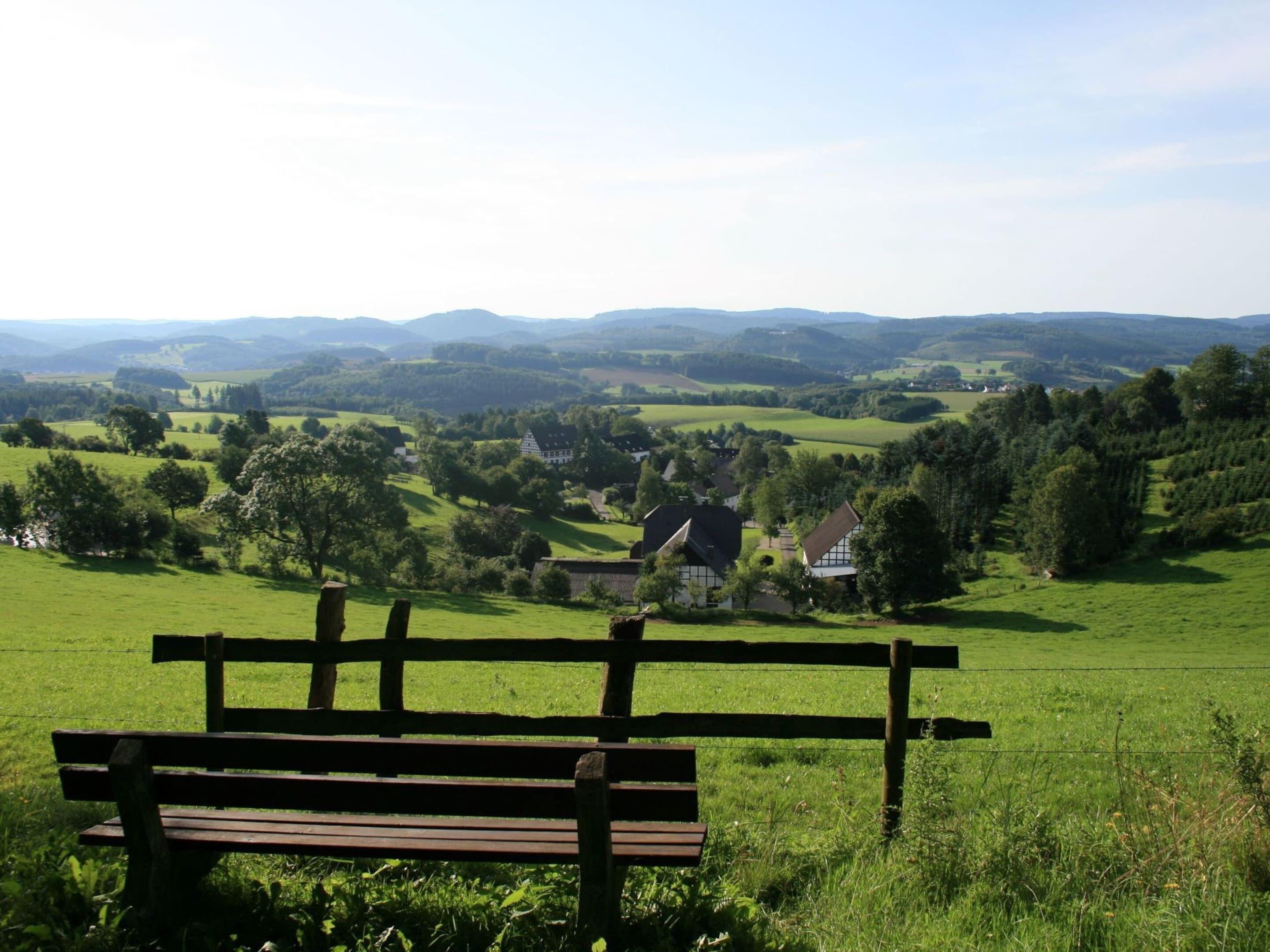A bench overlooking a rural landscape with houses and rolling hills in the distance.