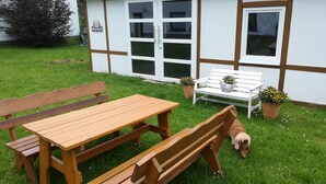 Un banco y una mesa de madera sobre un césped con un edificio blanco al fondo.
