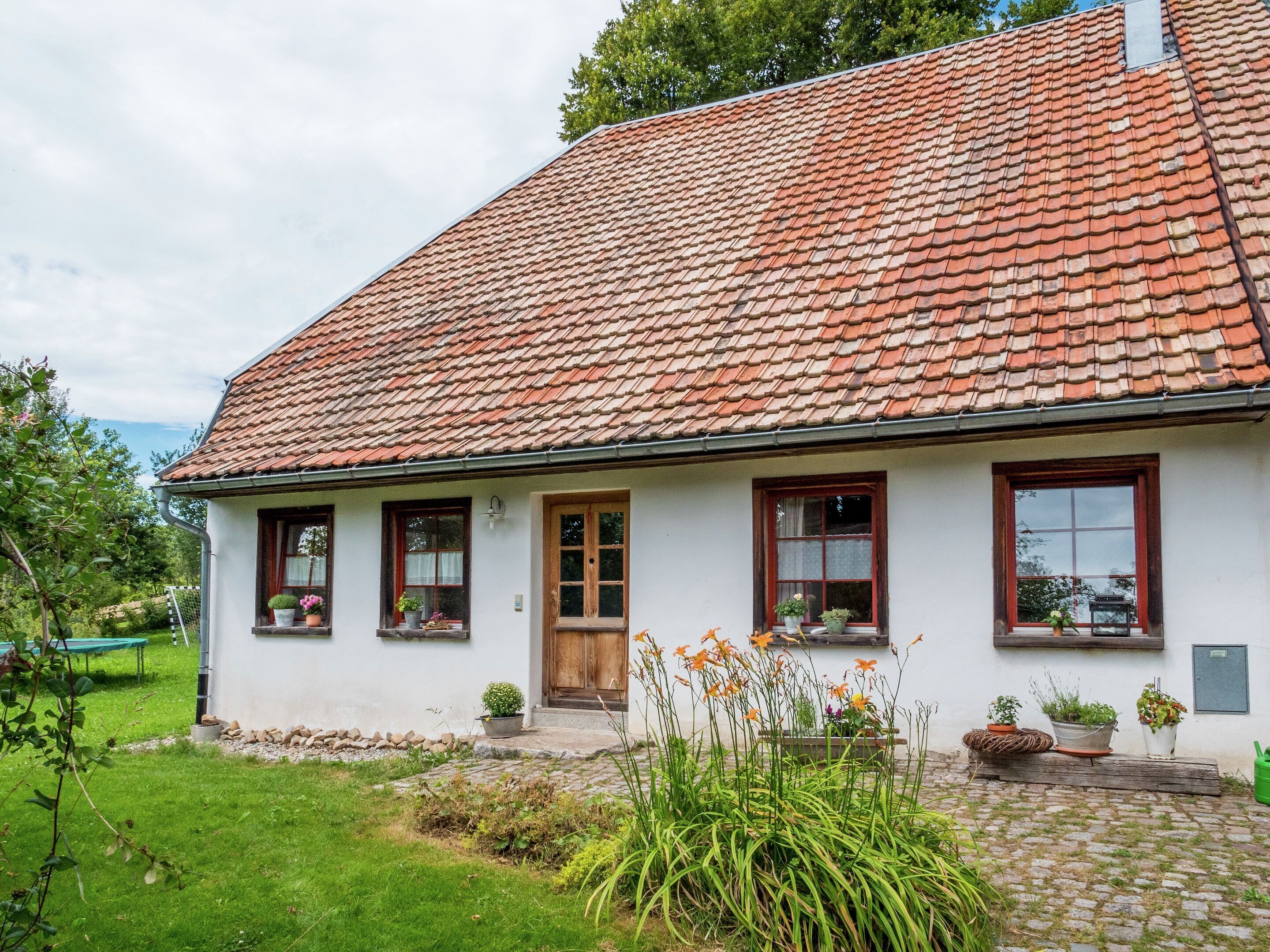 A white building with a red-tiled roof, a wooden door, and windows with dark frames.
