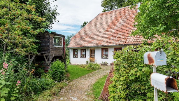 A cobblestone path leading to a white house with a red-tiled roof, surrounded by lush greenery and a wooden structure to the left. - Ferienhaus in Herrischried (Herrischried)