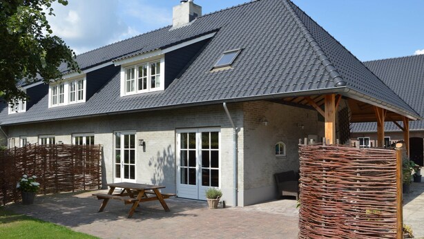 Ein Haus mit einem Ziegeldach, einer überdachten Terrasse und einem Holzzaun.