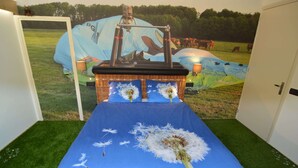 Ein Zimmer mit einem großen Bett, einem Korbhaupt und einer blauen Bettdecke mit einem Löwenzahnmuster.