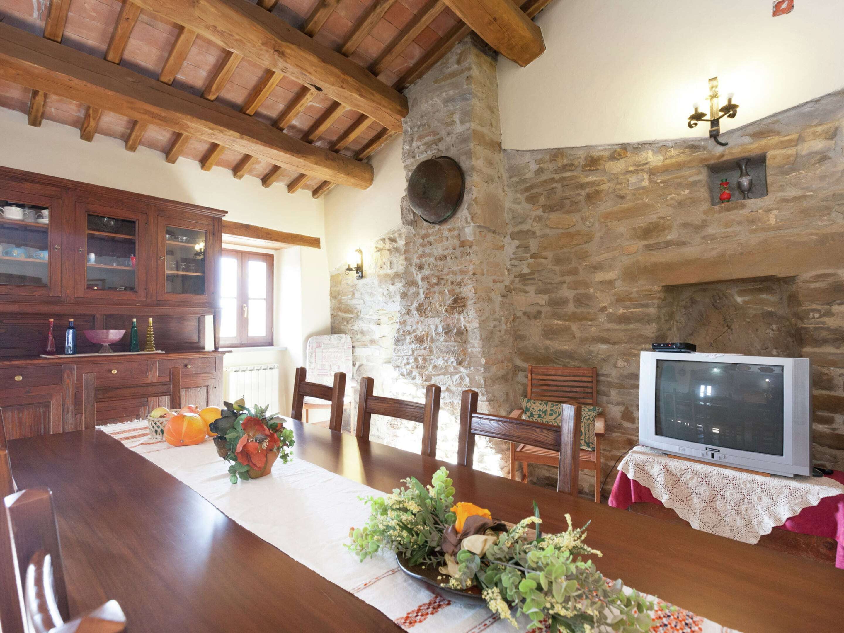 A rustic dining area with a wooden table, chairs, and a stone wall.