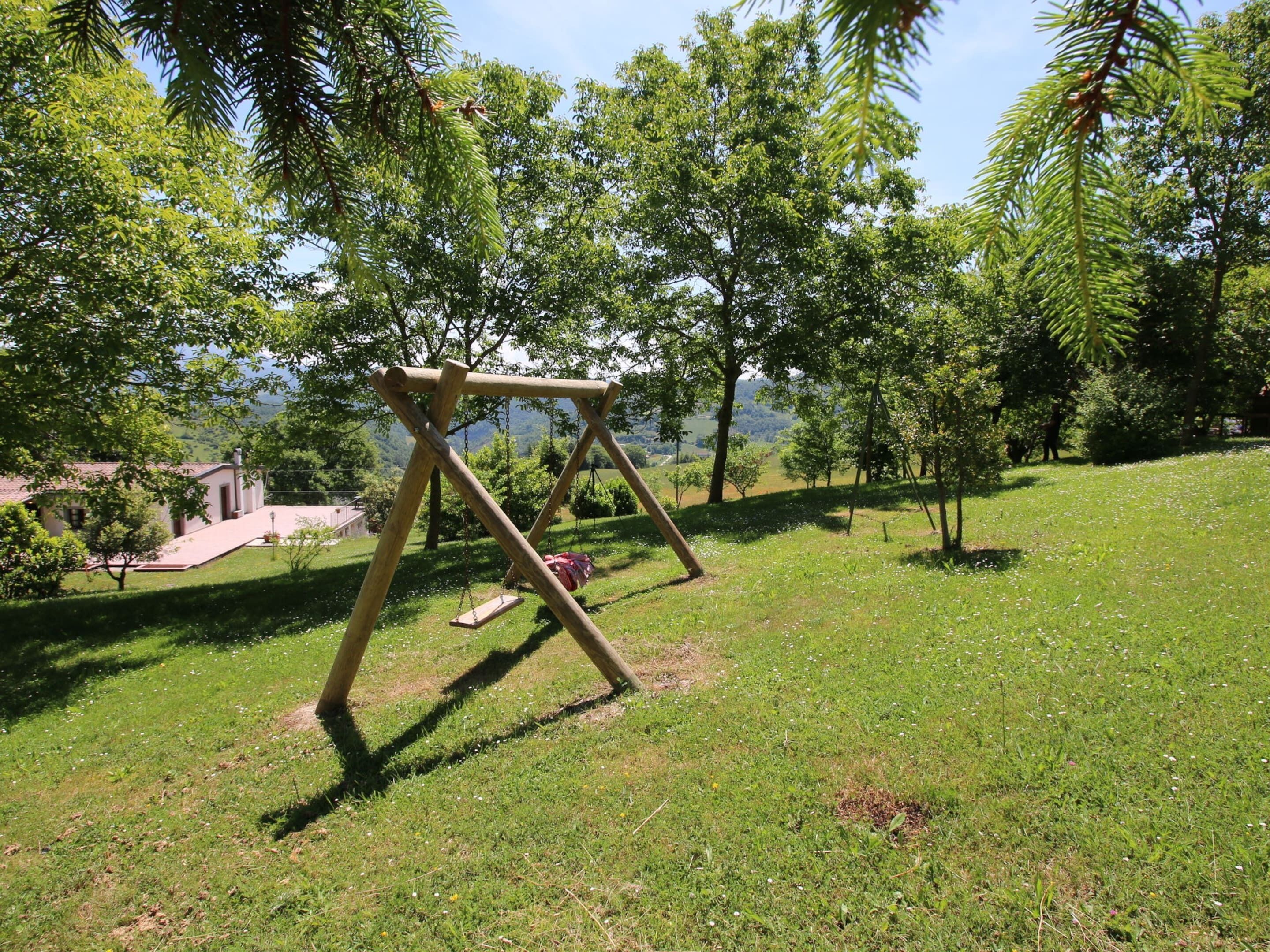 A wooden swing set in a grassy park area with trees and a building in the background.