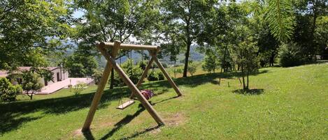 A wooden swing set in a grassy park area with trees and a building in the background.