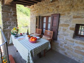 Habitación con paredes de piedra y una mesa para dos, con mantel a cuadros, un frutero y un florero.