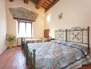Een slaapkamer met een bed, een raam, een nachtkastje, een lamp en een bloemenvaas.
