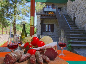 A rustic outdoor dining setup with a stone building in the background, a wooden table with food and wine, and a staircase leading to a balcony. - Belvilla by OYO Farmhouse With Swimming Pool (Apecchio)