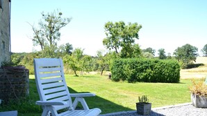 A white outdoor chair in a garden with a hedge and trees in the background.