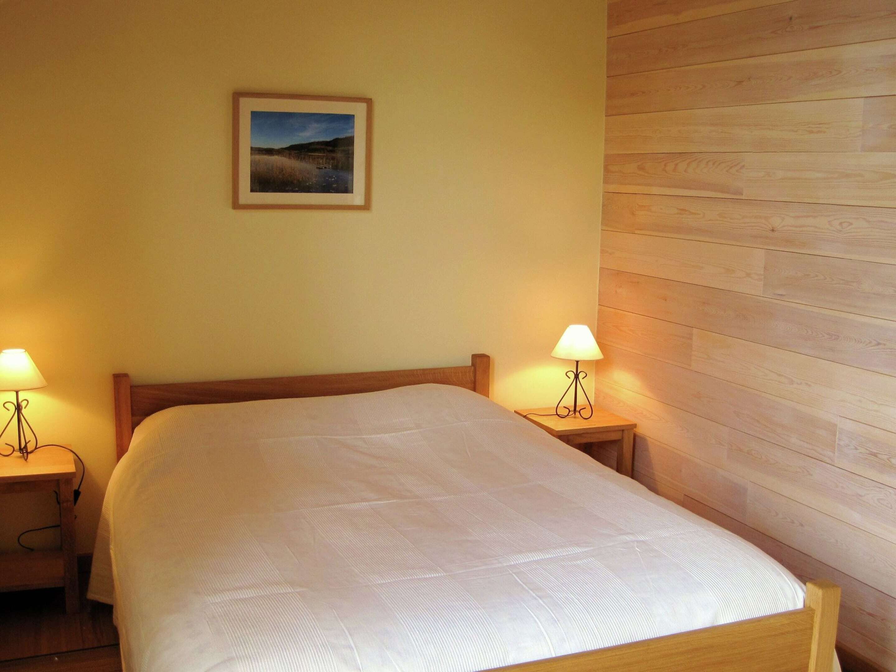 A neatly made bed with a wooden headboard, two bedside tables with lamps, and a framed picture on the wall.