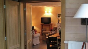 A room with a wooden door, a dining area with a table and chairs, a television on a stand, and a lamp. - Fort-like Holiday Home in Sart-bertrix, Near Luxembourg (Bertrix)