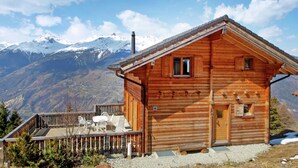 Eine Holzhütte mit Balkon, Schornstein und Blick auf schneebedeckte Berge.