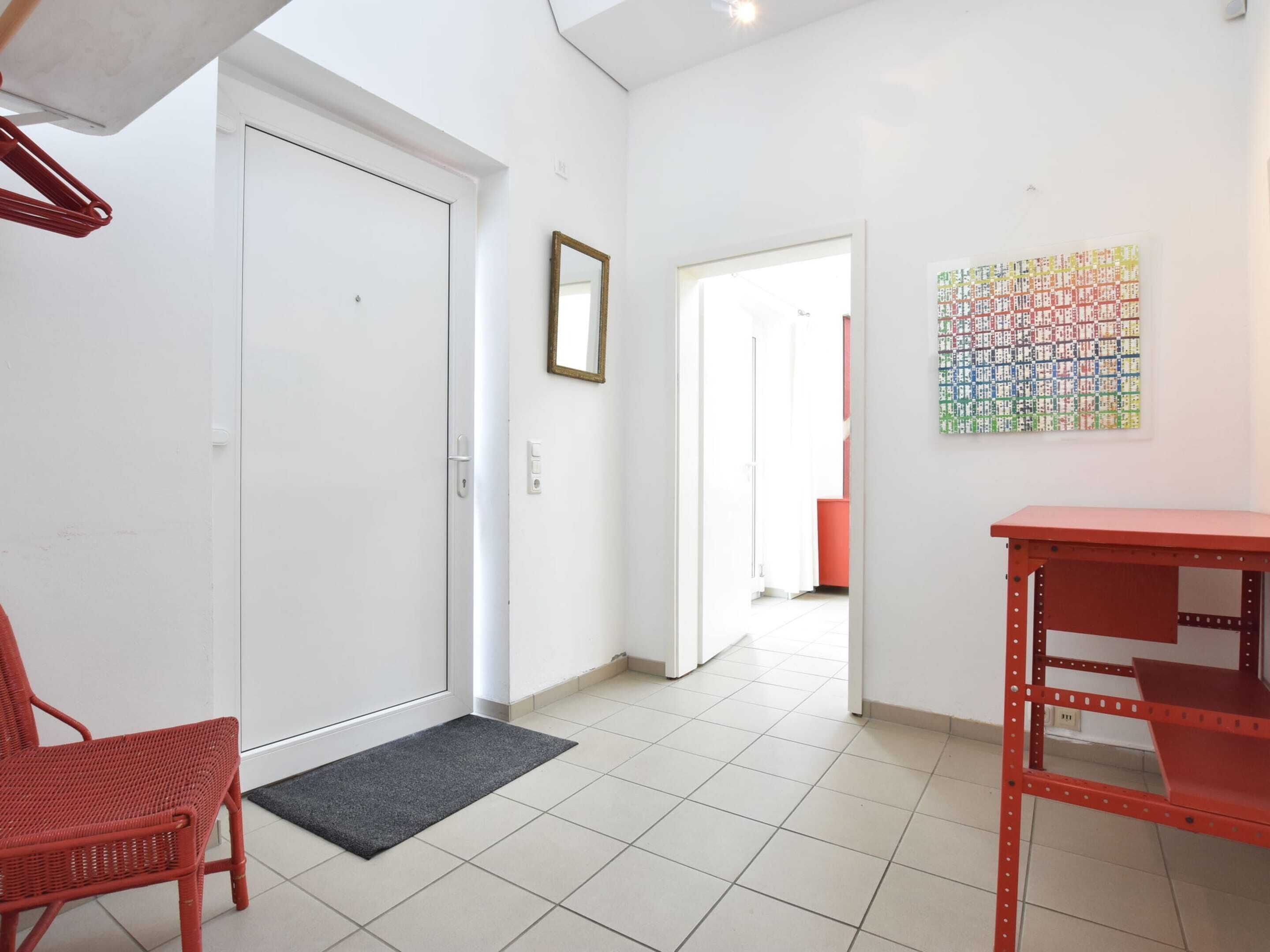 A hallway with a white door, a red chair, a red table, and a colorful artwork on the wall.